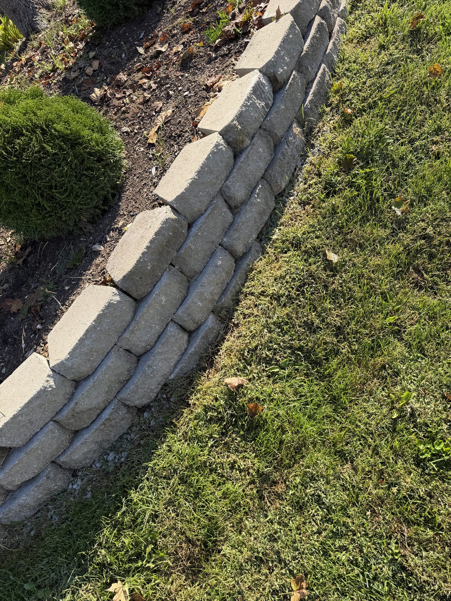 Stacked stone retaining wall edging along a landscape bed